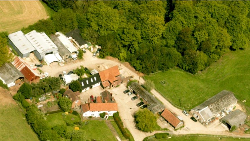 Aerial view of Cholsey Grange Farm, showing the farmhouse, listed oak-framed barn and converted outbuildings set among fields and woodland.